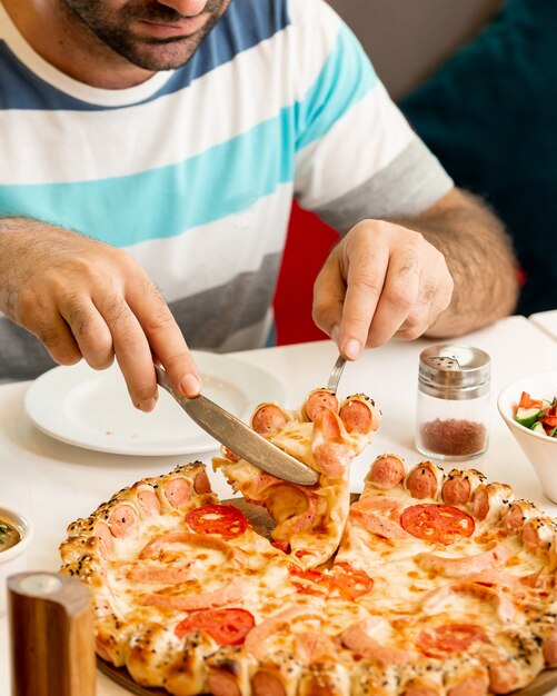 Hombre tomando una rebanada de pizza de salchicha