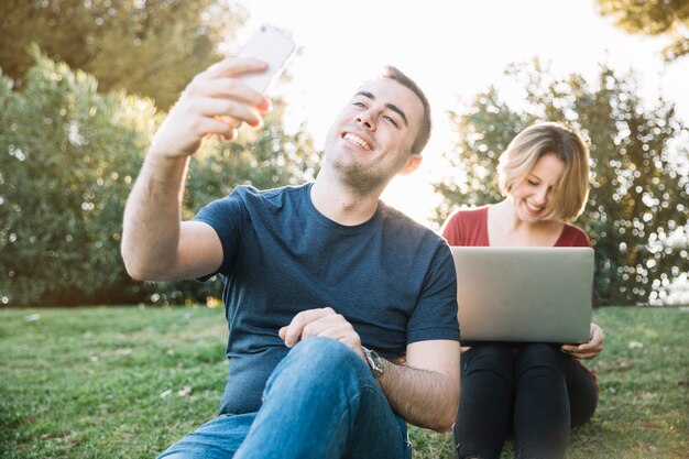 Hombre tomando selfie cerca de mujer con laptop