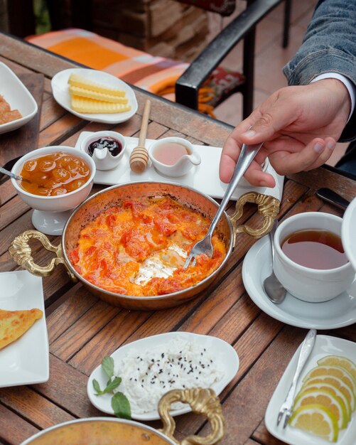 Hombre tomando tomate y huevo con tenedor en el desayuno tradicional