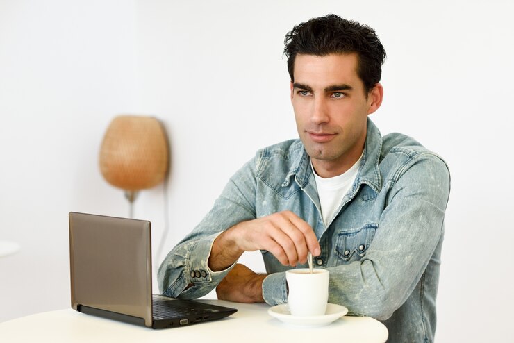 Foto gratuito hombre tomándose un café con un portátil al lado