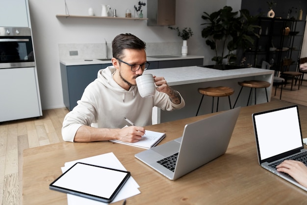 Hombre trabajando desde casa en el escritorio mientras toma una copa