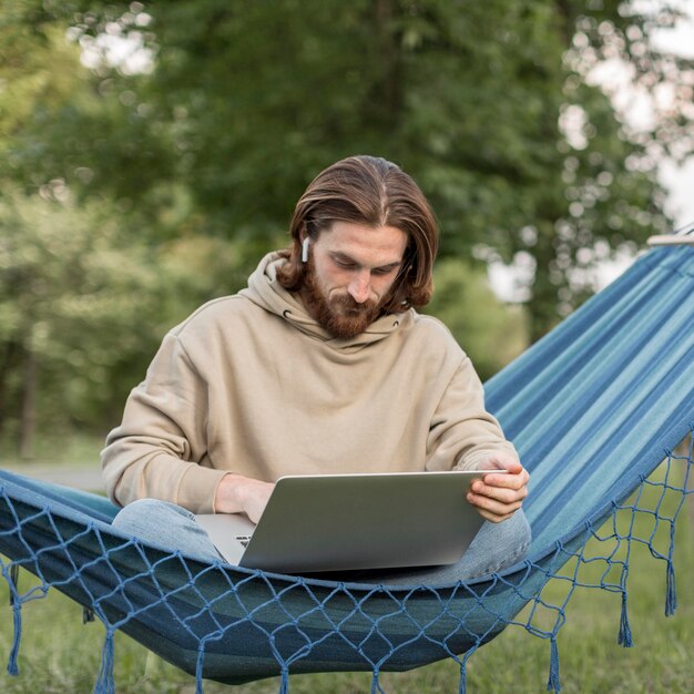 Hombre trabajando en la computadora portátil mientras está en la hamaca