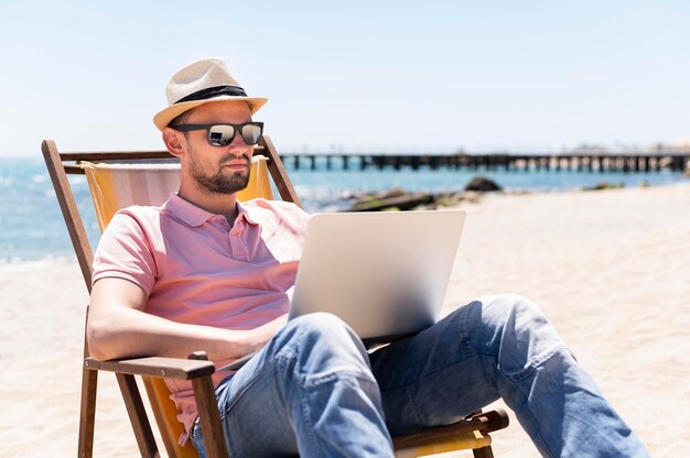 Hombre trabajando en la computadora portátil en la silla de playa