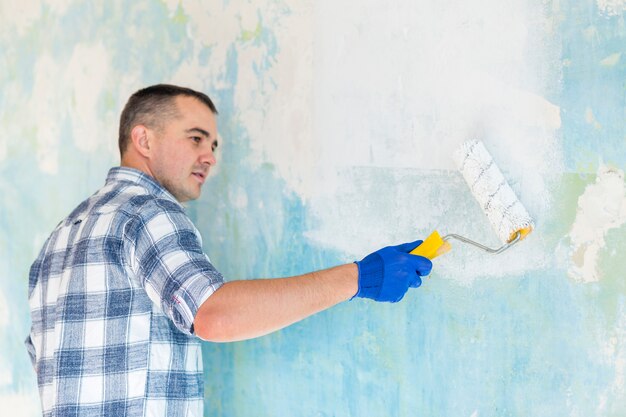 Hombre trabajando en una pared con rodillo de pintura