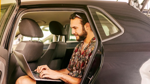 Hombre trabajando remotamente en el asiento trasero del carro