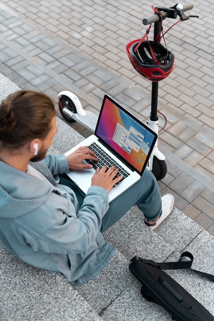 Foto gratuita hombre trabajando en su computadora portátil junto a su scooter