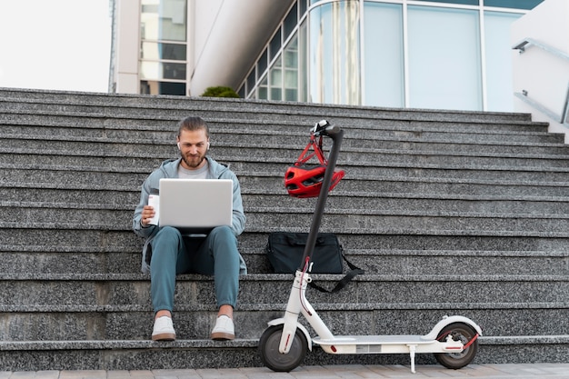 Hombre trabajando en su computadora portátil junto a su scooter