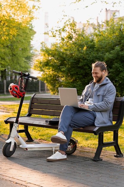 Hombre trabajando en su computadora portátil junto a su scooter