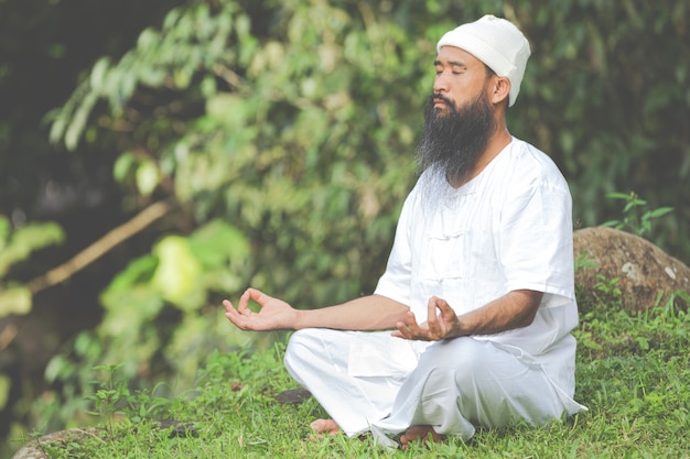 Hombre en traje blanco meditando en la naturaleza