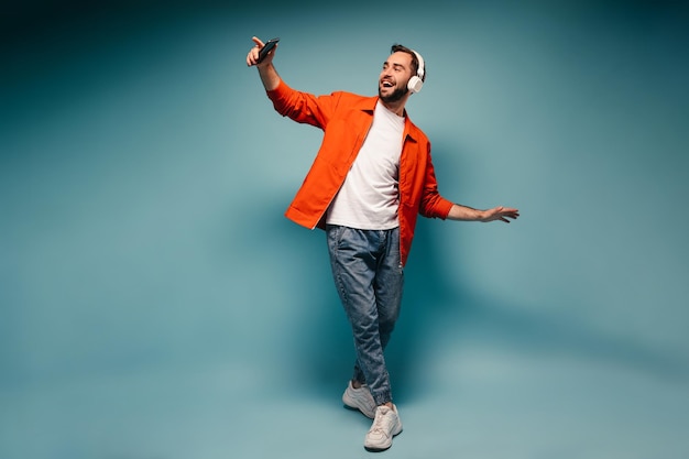 Foto gratuita hombre en traje elegante bailando sobre fondo azul y sosteniendo el teléfono inteligente