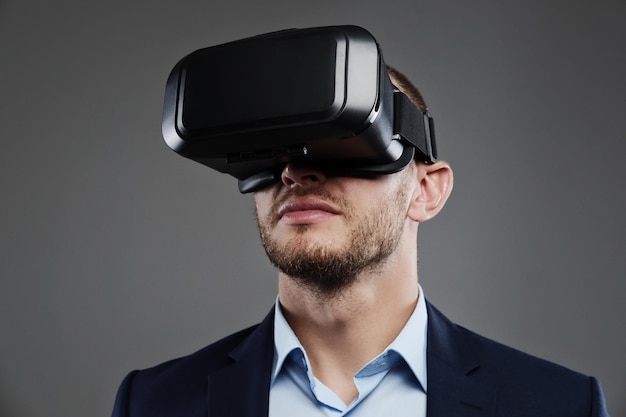 Hombre con traje y gafas de realidad virtual en la cabeza. Aislado sobre fondo gris.