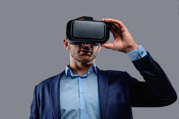 Hombre con traje y gafas de realidad virtual en la cabeza. Aislado sobre fondo gris.