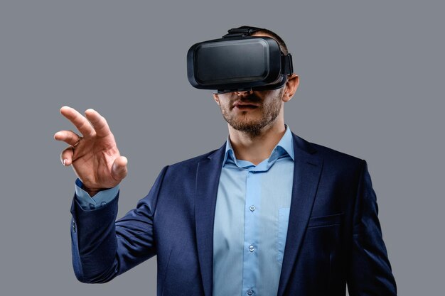 Hombre con traje y gafas de realidad virtual en la cabeza. Aislado sobre fondo gris.