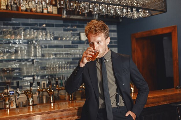 El hombre con un traje negro bebe alcohol. Chico atractivo bebe whisky de un vaso.