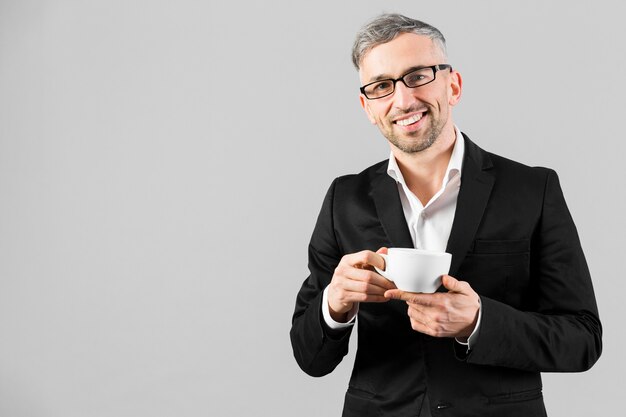 Hombre de traje negro con gafas y sosteniendo un café