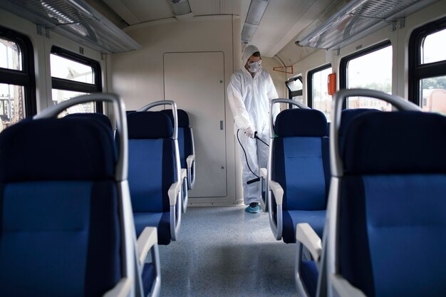 Hombre con traje de protección blanco desinfectando y desinfectando el interior del tren subterráneo para detener la propagación del virus corona altamente contagioso