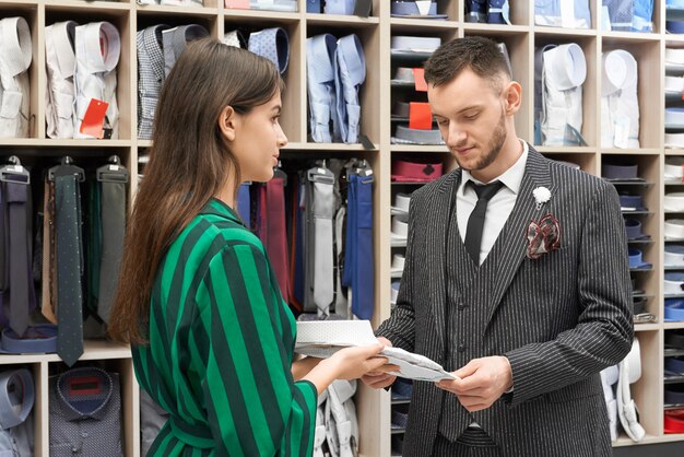 Hombre en traje de rayas elegir camisa, asistente proponiendo.