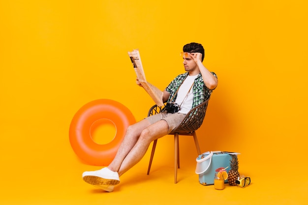 El hombre en traje de verano se quita las gafas y lee el periódico. Retrato de chico en espacio naranja con maleta y anillo de goma.