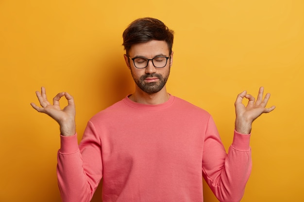 Hombre tranquilo barbudo relajado hace yoga, respira profundamente, cierra los ojos