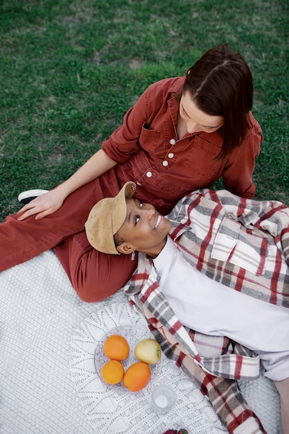 Hombre trans manteniendo la cabeza en el regazo de su novia mientras hace un picnic en el parque