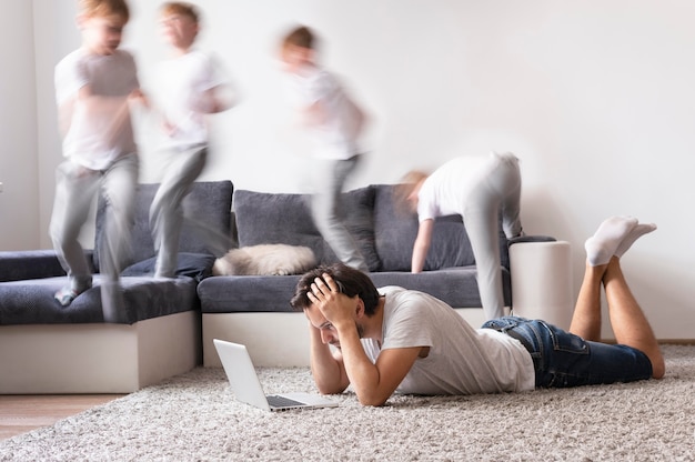 Foto gratuita hombre tratando de trabajar en la computadora portátil desde casa mientras sus hijos corren