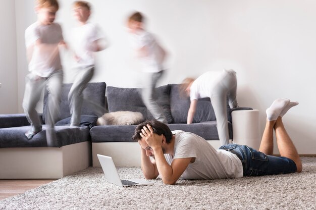 Hombre tratando de trabajar en la computadora portátil desde casa mientras sus hijos corren