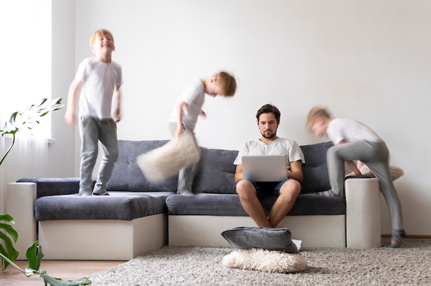 Hombre tratando de trabajar en la computadora portátil desde casa mientras sus hijos corren
