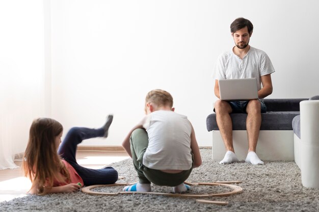 Hombre tratando de trabajar en la computadora portátil desde casa mientras sus hijos corren