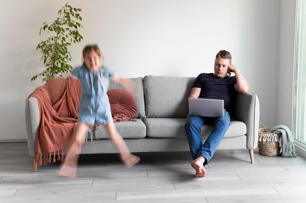 Hombre tratando de trabajar en la computadora portátil desde casa mientras sus hijos corren