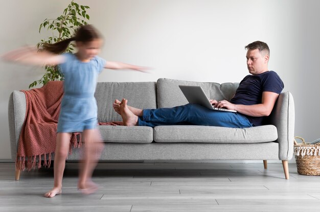 Hombre tratando de trabajar en la computadora portátil desde casa mientras sus hijos corren