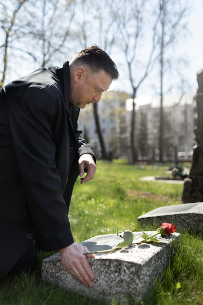 Foto gratuita hombre trayendo una rosa a una lápida en el cementerio