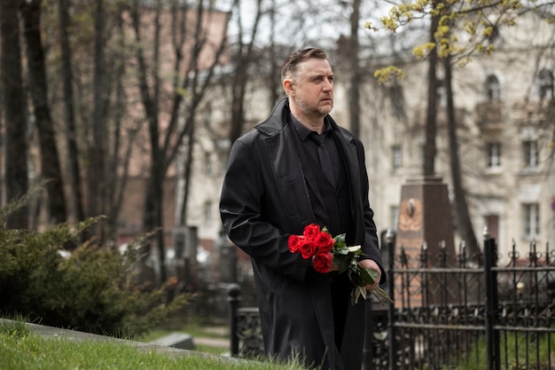 Foto gratuita hombre trayendo rosas a una lápida en el cementerio