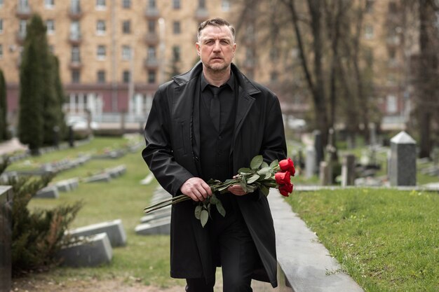 Foto gratuita hombre trayendo rosas a una lápida en el cementerio