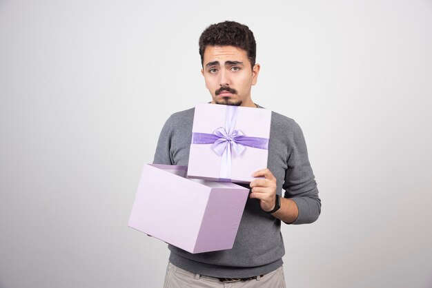 Hombre triste abriendo una caja violeta sobre una pared blanca.