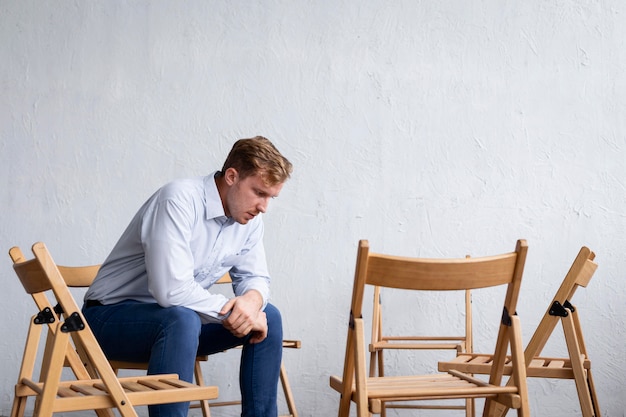 Hombre triste en una sesión de terapia de grupo con sillas vacías