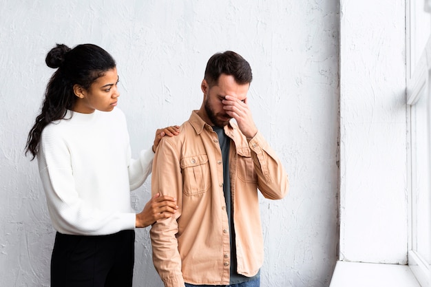 Hombre triste siendo consolado por mujer en una sesión de terapia de grupo