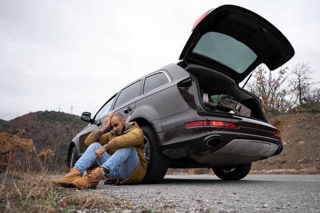 Hombre triste de tiro completo sentado cerca del auto