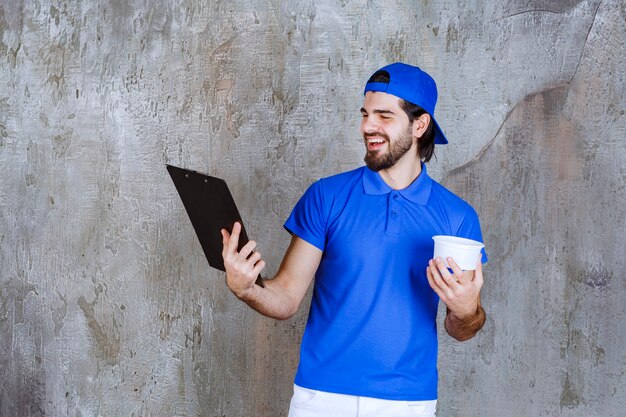 Hombre de uniforme azul sosteniendo un vaso de plástico para llevar y leyendo el nombre del cliente.