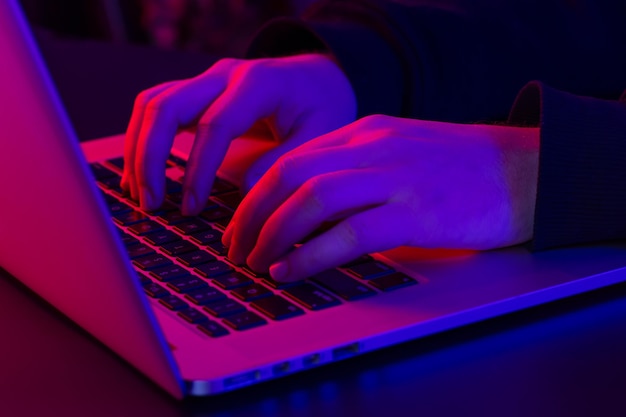 Un hombre usa una computadora portátil con las manos masculinas en primer plano con luces de neón