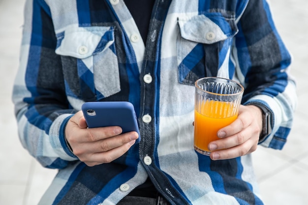 Un hombre usa un teléfono inteligente y bebe jugo de naranja.