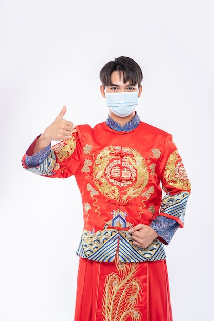 El hombre usa traje Cheongsam y máscara muestra la mejor manera de comprar para proteger la enfermedad