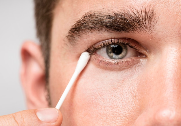 Hombre usando un bastón para la oreja para limpiar su ojo