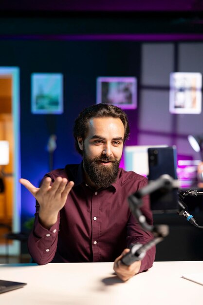 Hombre usando cámara de teléfono para grabar vlog en apartamento para canal de podcasting