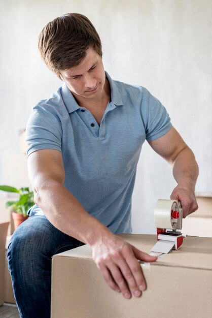 Hombre usando cinta adhesiva para empaquetar la caja para mudarse