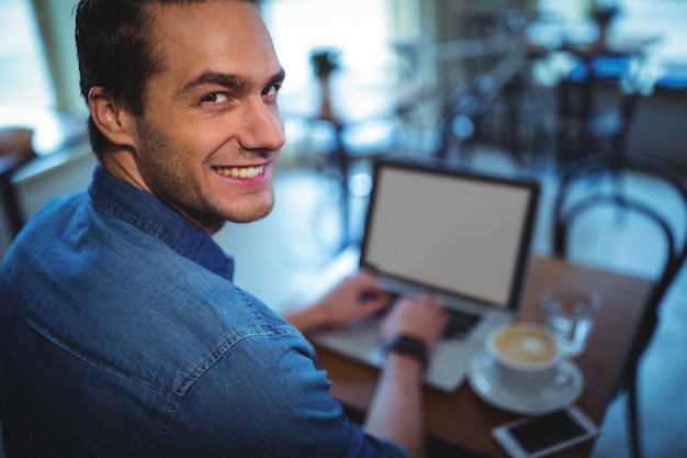 El hombre usando la computadora portátil mientras que el café en la cafetería ©