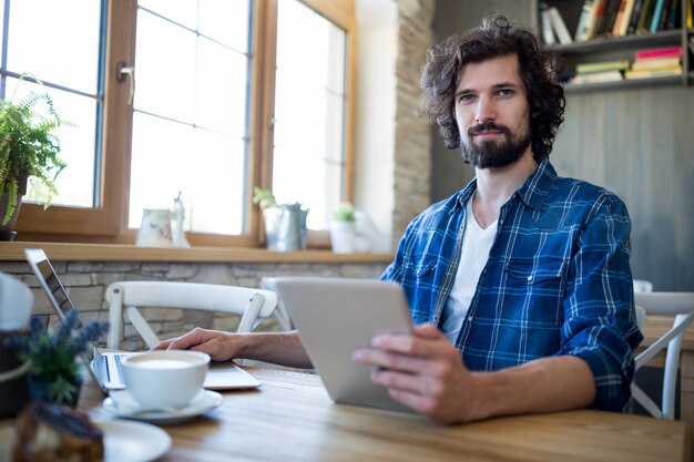 El hombre usando la computadora portátil y la tableta digital en la tienda de café