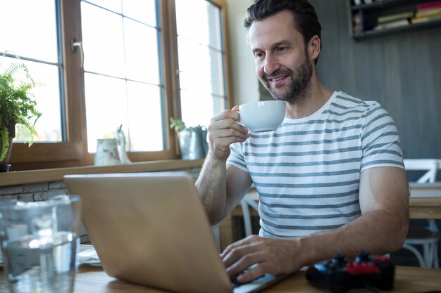 El hombre usando la computadora portátil y tener una taza de café en la cafetería