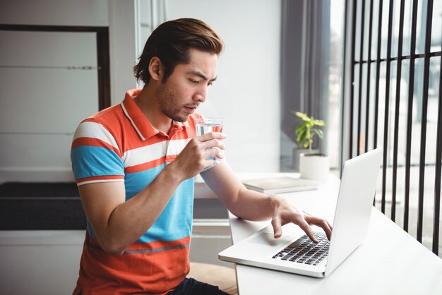 Hombre usando laptop mientras bebe agua