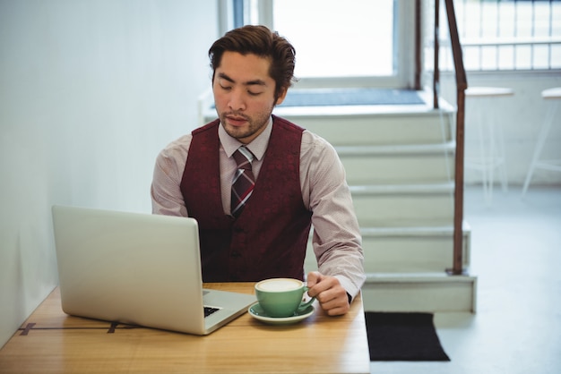 Hombre usando laptop mientras toma café