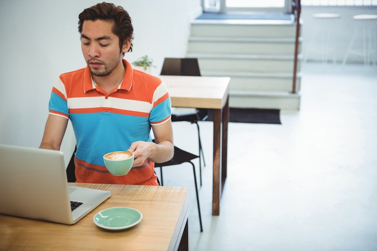 Foto gratuito hombre usando laptop mientras toma una taza de café